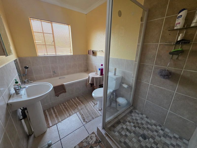 A functional bathroom featuring a pedestal basin, a built-in bathtub, and a separate shower enclosure with tiled finishes.