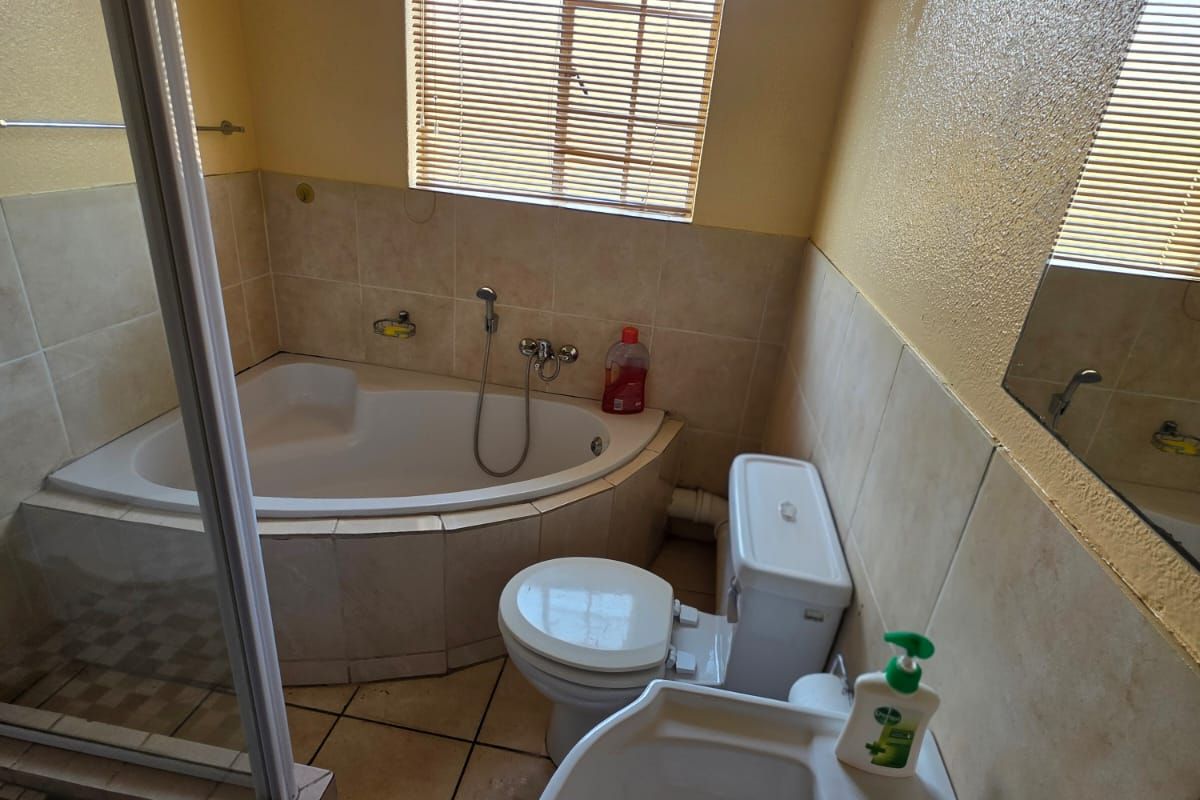 A functional bathroom featuring a corner bathtub, separate shower enclosure, pedestal basin, and toilet with neutral wall and floor tiling.