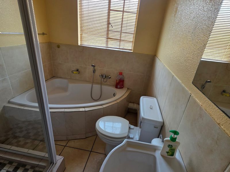 A functional bathroom featuring a corner bathtub, separate shower enclosure, pedestal basin, and toilet with neutral wall and floor tiling.