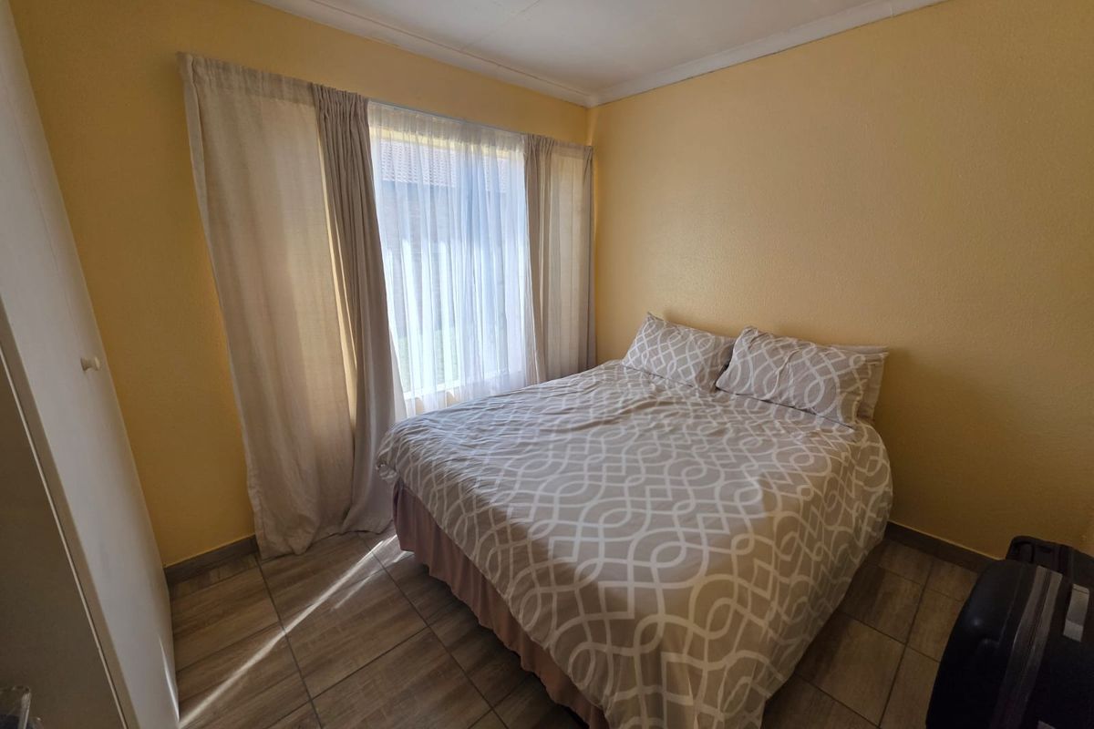 A functional bedroom featuring tiled flooring, a built-in cupboard, and natural light through large windows with curtain rails.