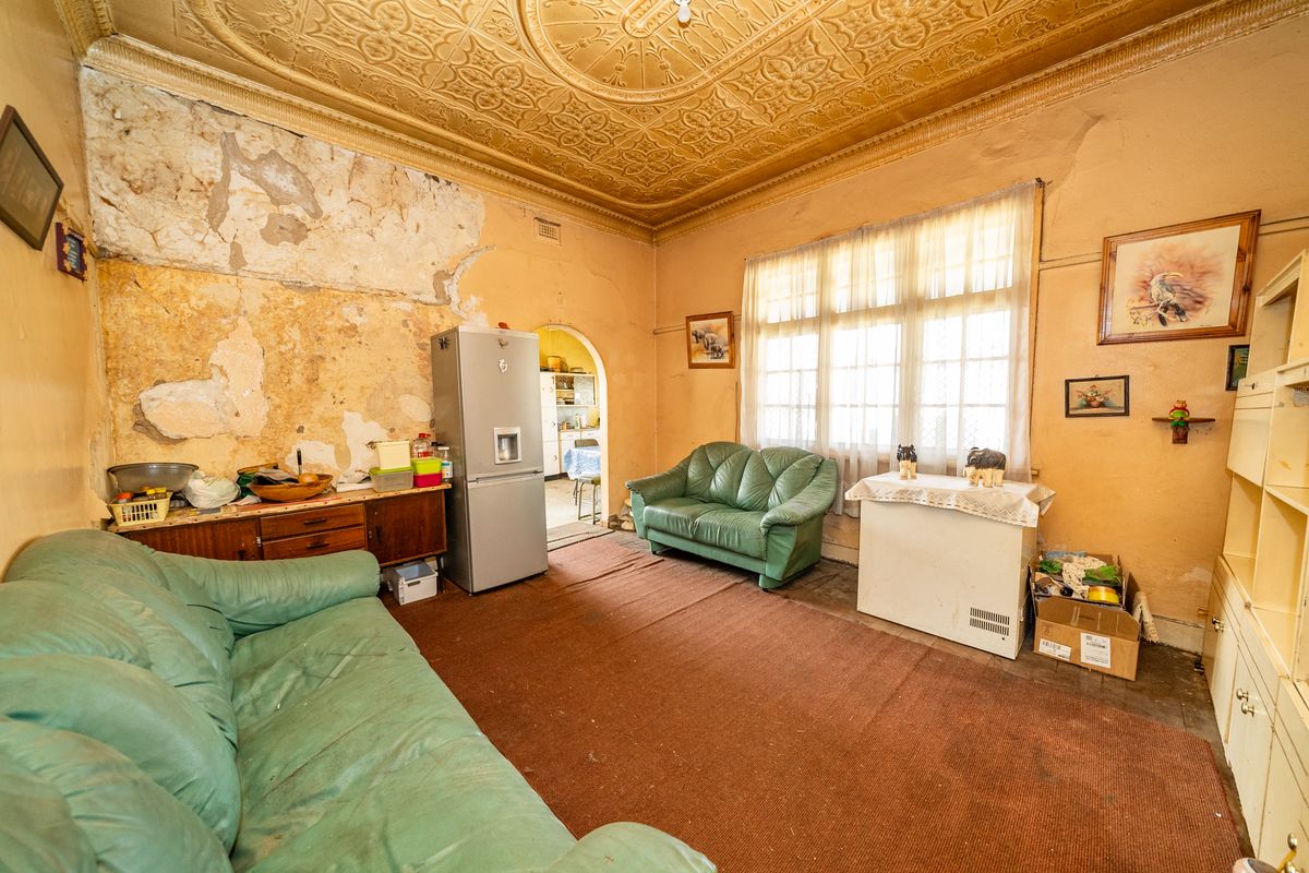 Living room featuring an ornate pressed metal ceiling and an archway leading to the kitchen, requiring significant renovation and plaster repair.