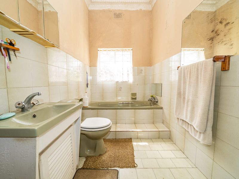 A dated bathroom featuring a built-in vanity, basin, toilet, and bathtub with tiled finishes, requiring cosmetic updates to modernize the space.