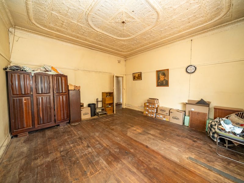 Spacious bedroom featuring original ornate pressed metal ceilings, timber floorboards, and classic picture rails, offering significant potential for renovation and restoration.