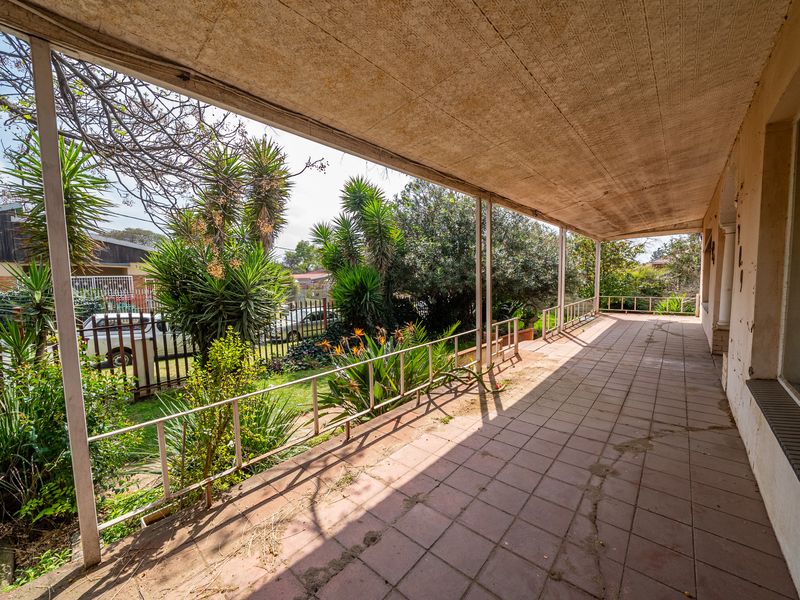 A covered outdoor patio area featuring tiled flooring, metal railings, and support columns, overlooking a garden space.