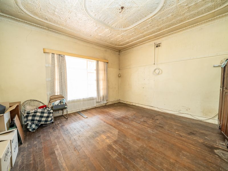 A spacious bedroom featuring original ornate pressed metal ceilings, timber floorboards, and classic picture rails, offering significant potential for renovation and restoration.