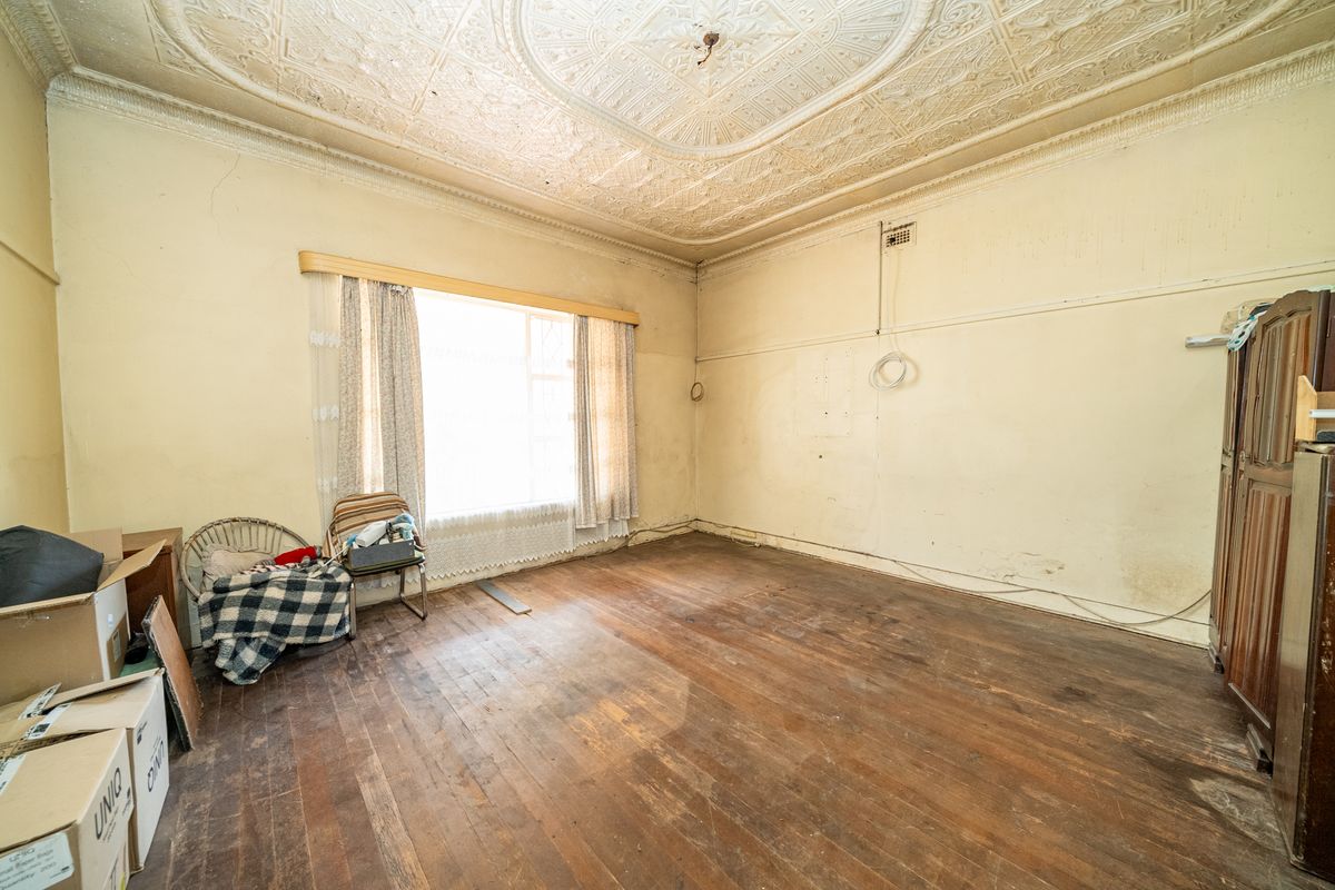 A spacious bedroom featuring original ornate pressed metal ceilings, timber floorboards, and classic picture rails, offering significant potential for renovation and restoration.