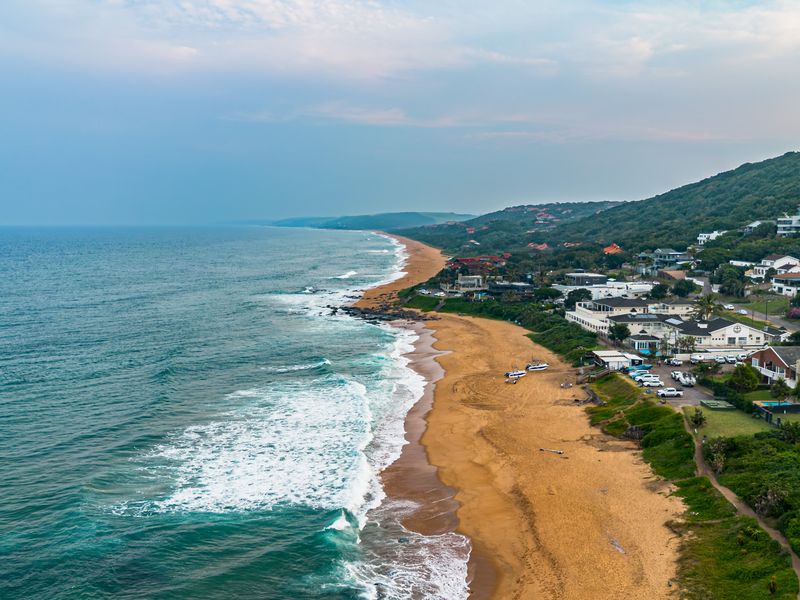 An aerial view of the coastal landscape, showcasing the beach, ocean, and surrounding residential properties along the coastline.