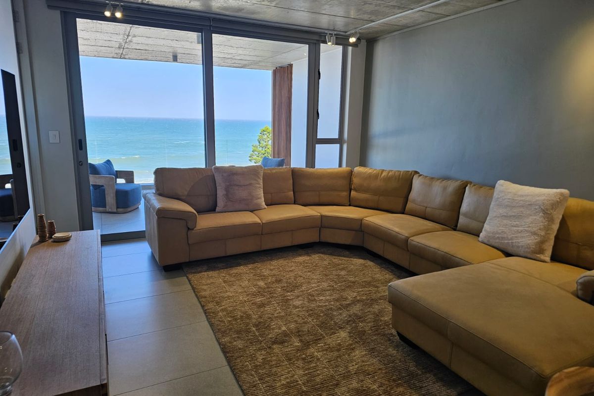 Modern living room featuring an exposed concrete ceiling, large sliding glass doors, and direct access to a balcony with expansive ocean views.