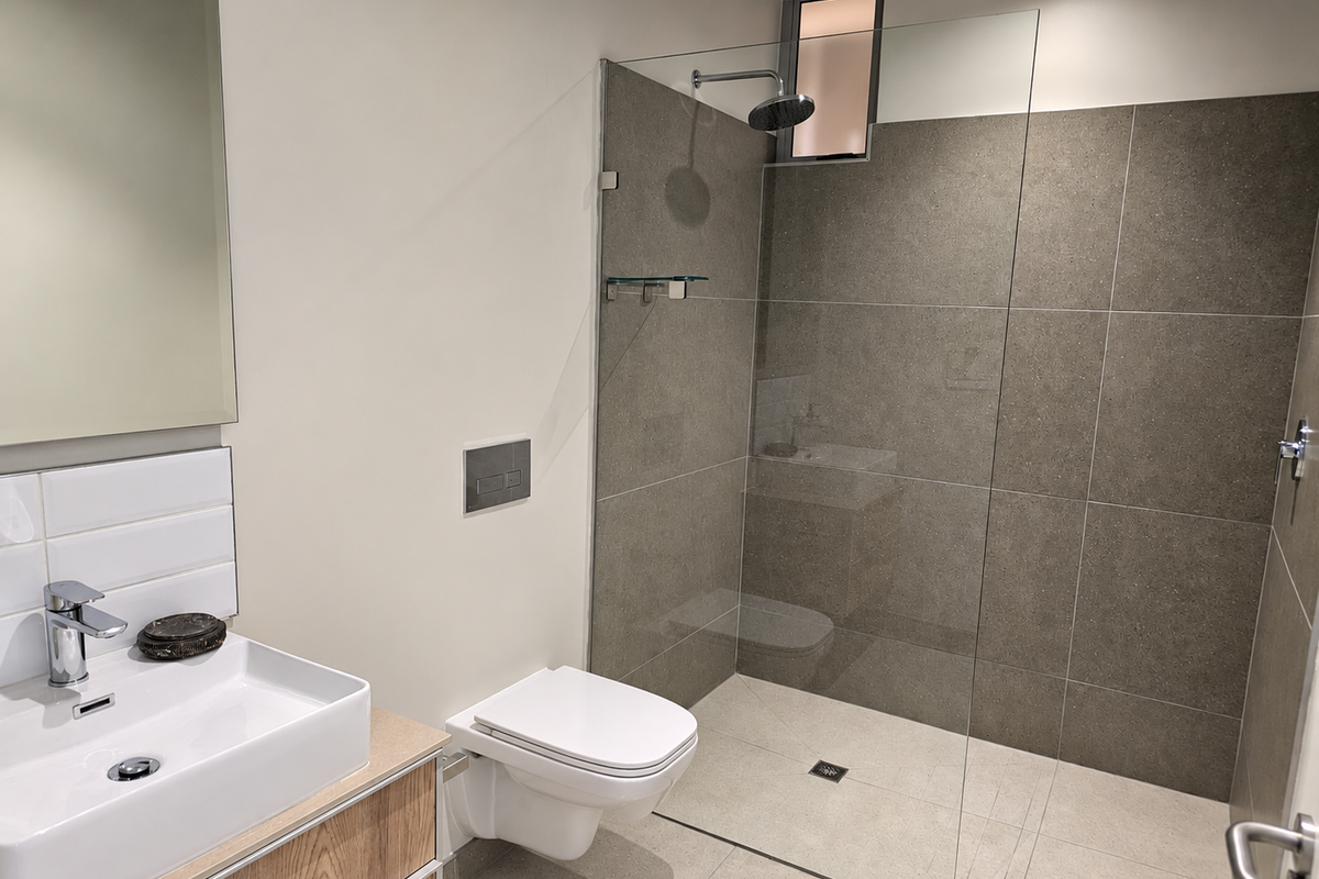 Modern bathroom featuring a wall-mounted toilet, a spacious walk-in shower with a glass screen, and a contemporary vanity basin.