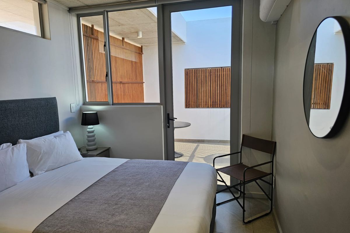 Modern bedroom featuring an exposed concrete ceiling, tiled flooring, and direct access to a private balcony through a glass door.