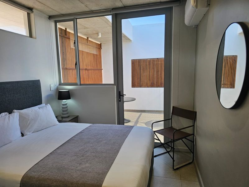 Modern bedroom featuring an exposed concrete ceiling, tiled flooring, and direct access to a private balcony through a glass door.
