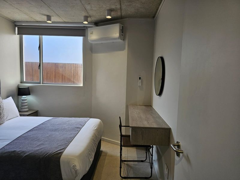 Modern bedroom featuring an exposed concrete ceiling, tiled flooring, a built-in floating desk, and a wall-mounted split-system air conditioner.