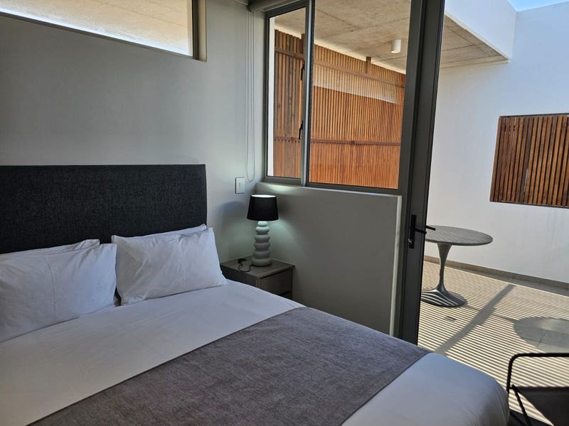 Modern bedroom featuring an exposed concrete ceiling, clerestory window, and direct access to a private outdoor patio with timber slat privacy screening.