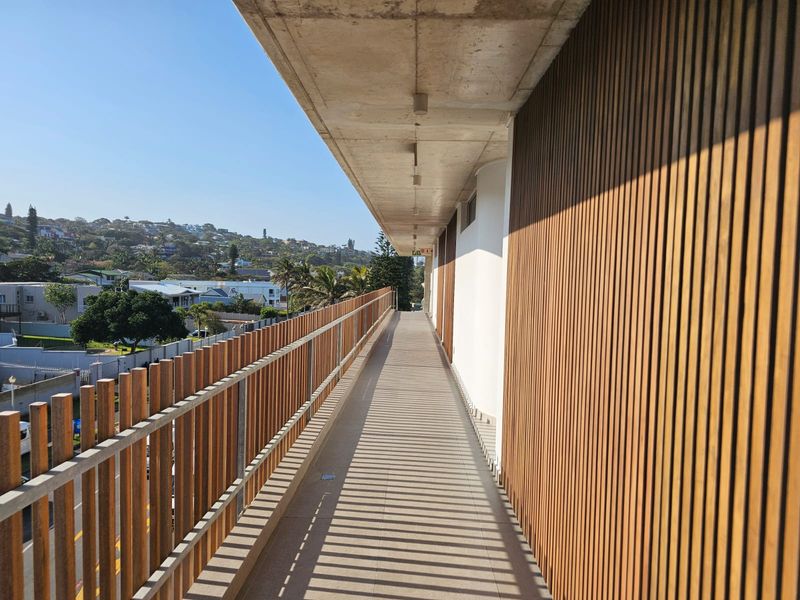 A modern, spacious balcony featuring timber slat cladding, a matching balustrade, and an exposed concrete ceiling with integrated lighting, offering elevated neighbourhood views.