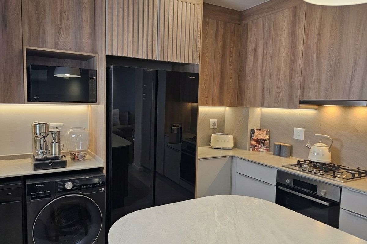Modern kitchen featuring wood-grain cabinetry, stone countertops, integrated appliances, gas hob, and a central island with under-cabinet lighting.
