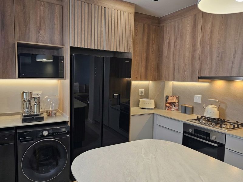 Modern kitchen featuring wood-grain cabinetry, stone countertops, integrated appliances, gas hob, and a central island with under-cabinet lighting.