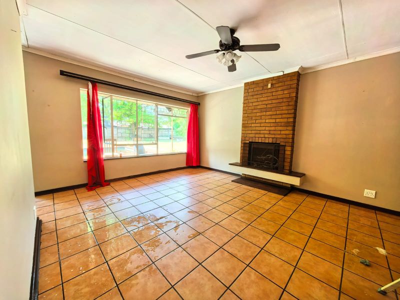 Spacious living room featuring a brick fireplace, ceiling fan, and tiled flooring. The room is vacant and ready for renovation.