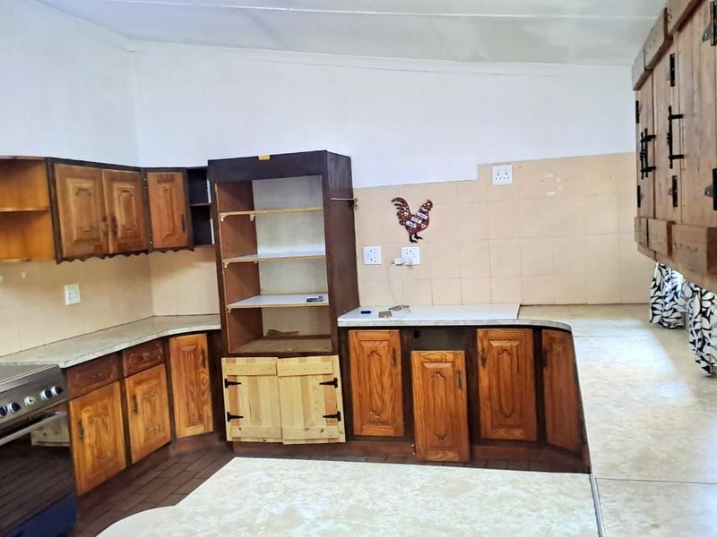 A dated kitchen featuring wooden cabinetry, tiled splashbacks, and a freestanding stove, offering significant potential for modernization and renovation.
