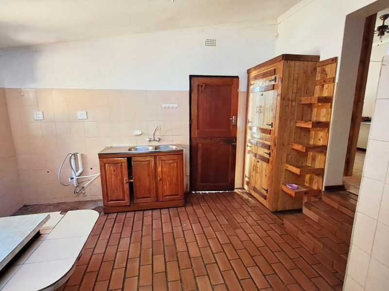 A functional kitchen area featuring brick flooring, a built-in sink unit, tiled splashbacks, and integrated timber cabinetry.