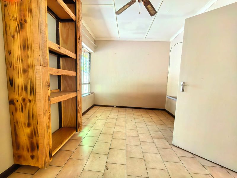 An empty bedroom featuring tiled flooring, a ceiling fan, and a built-in wooden shelving unit with security bars on the window.