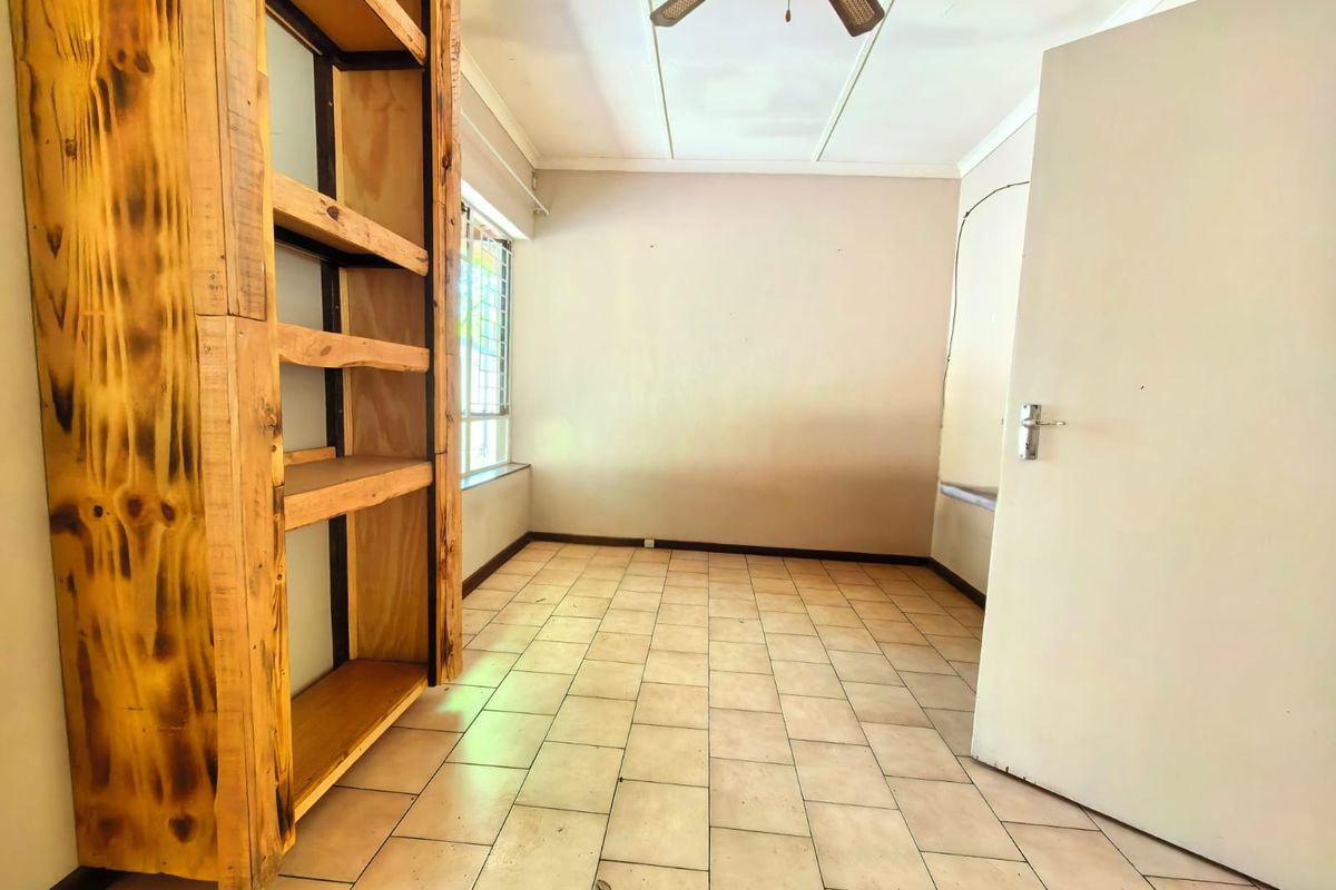 An empty bedroom featuring tiled flooring, a ceiling fan, and a built-in wooden shelving unit with security bars on the window.