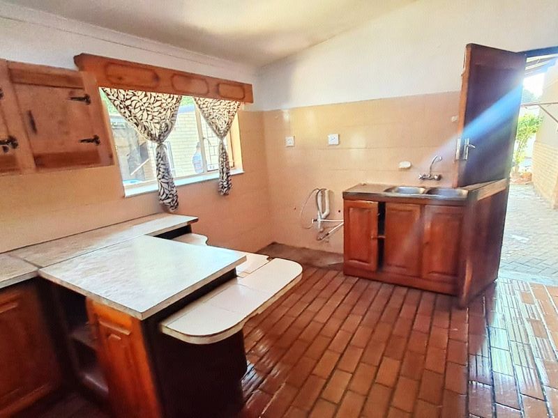 A dated kitchen featuring wooden cabinetry, brick flooring, and a stable door leading to an outdoor area, offering significant potential for renovation.