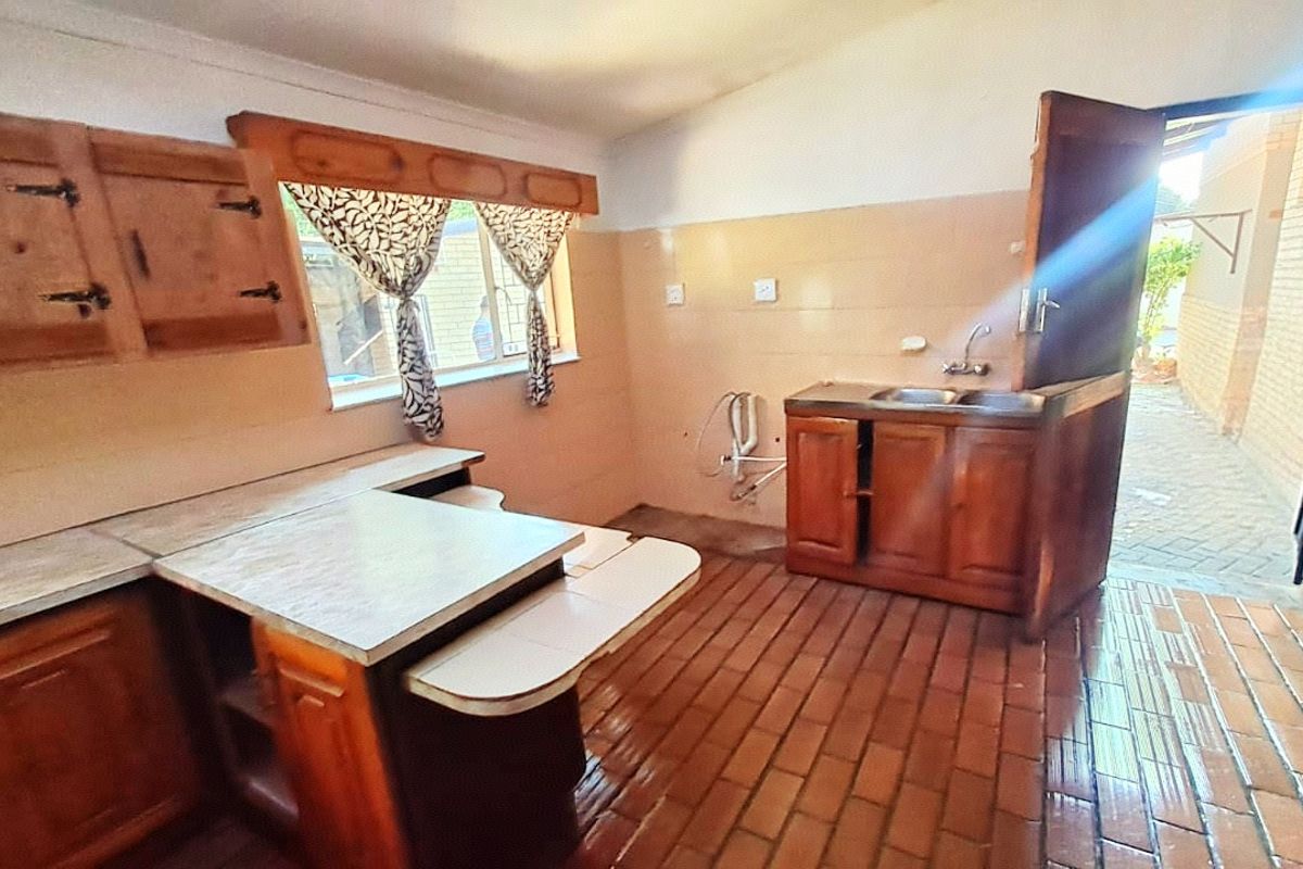 A dated kitchen featuring wooden cabinetry, brick flooring, and a stable door leading to an outdoor area, offering significant potential for renovation.
