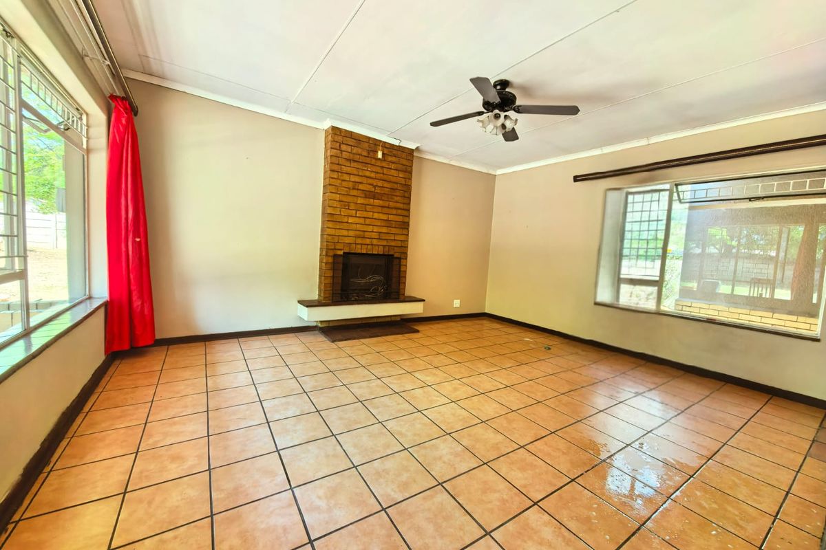 Spacious living room featuring a brick fireplace, tiled flooring, and ceiling fan, offering a blank canvas for renovation and interior design updates.