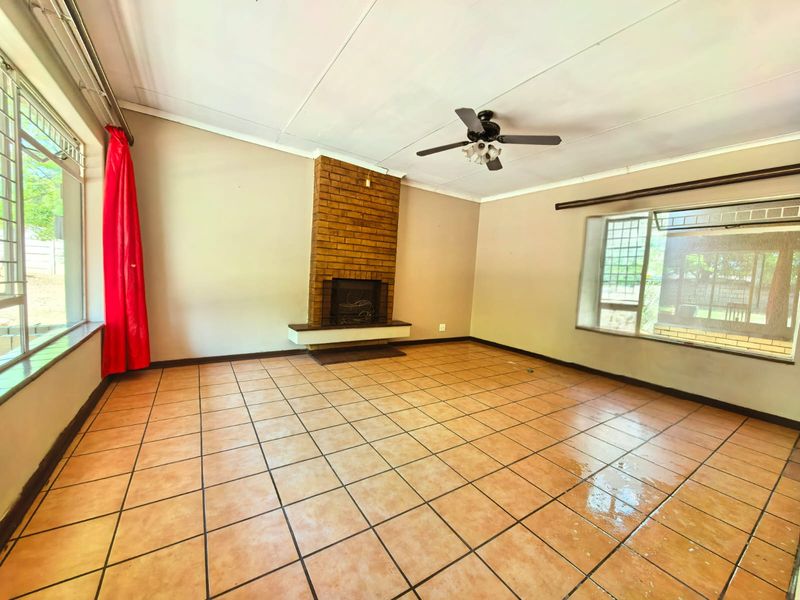 Spacious living room featuring a brick fireplace, tiled flooring, and ceiling fan, offering a blank canvas for renovation and interior design updates.
