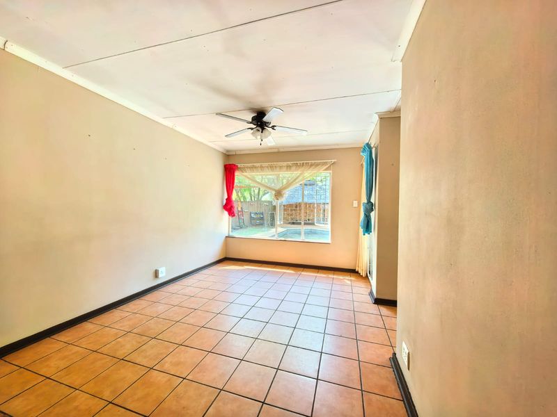 A spacious, empty living room featuring tiled flooring, a ceiling fan, and a large window overlooking the backyard pool area.