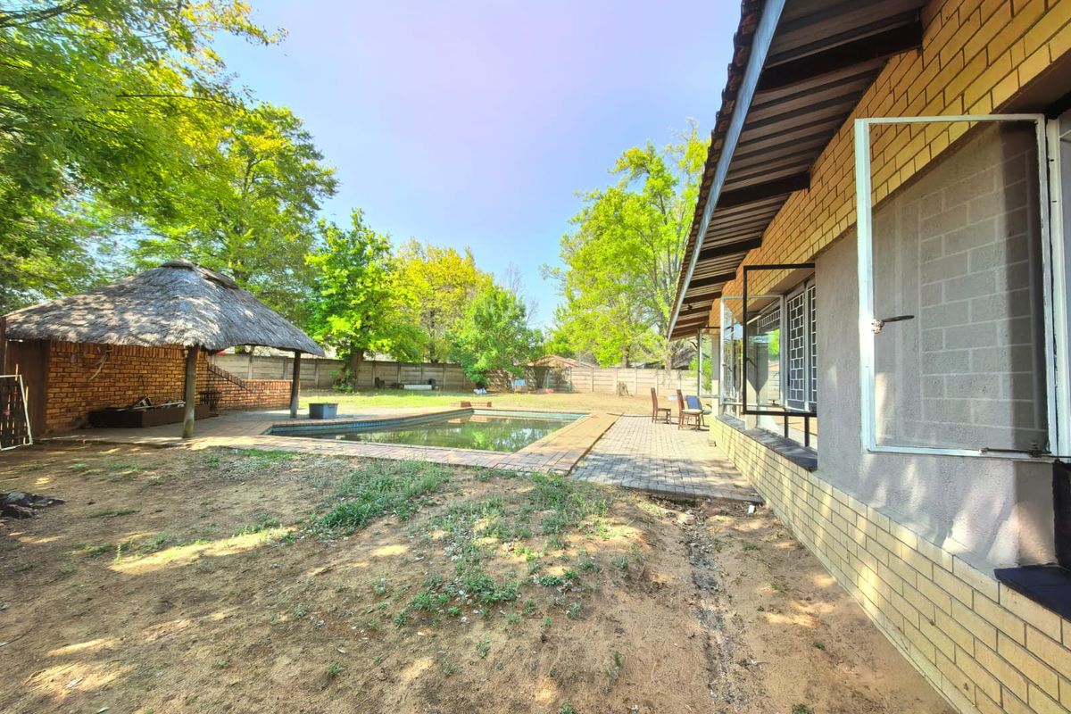 Rear exterior view featuring a swimming pool, a thatch lapa, and a paved patio area adjacent to the main house structure.