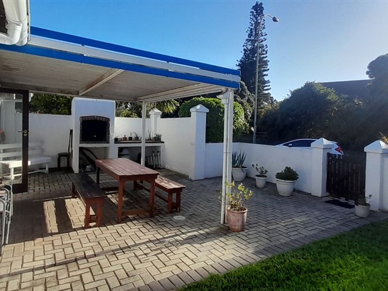 A paved outdoor patio area featuring a built-in braai, covered pergola structure, and enclosed boundary walls, suitable for outdoor entertaining.