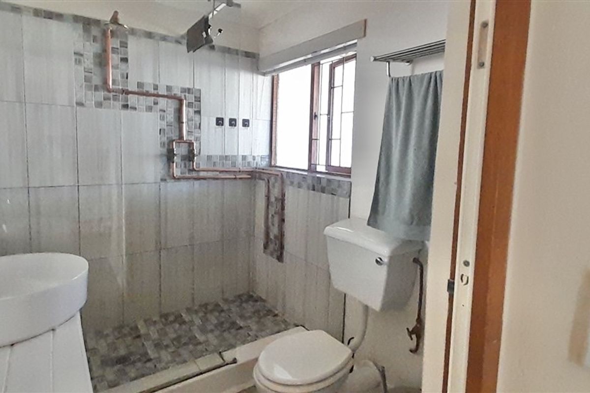 A functional bathroom featuring a vessel sink, a tiled shower enclosure with exposed copper plumbing, and a standard toilet.