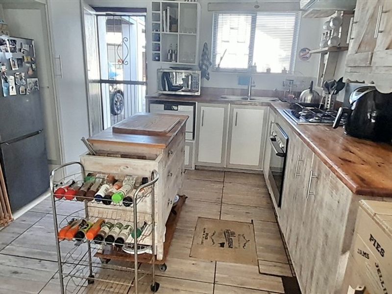 A functional kitchen featuring wooden countertops, built-in cabinetry, a gas hob, and tiled flooring, with direct access to the exterior via a security gate.
