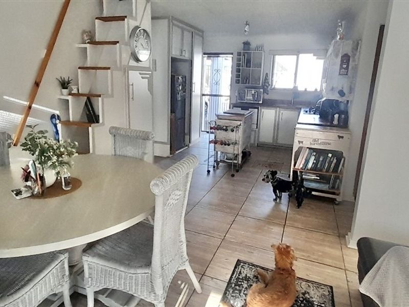 Open plan living and dining area featuring tiled flooring and a compact kitchen with built-in cabinetry and staircase access.