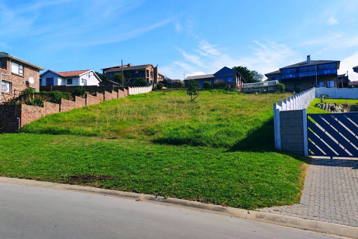 A vacant residential plot featuring a gentle slope, established grass, and existing boundary walls with a gated driveway entrance.