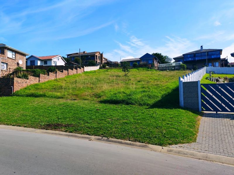 A vacant residential plot featuring a gentle slope, established grass, and existing boundary walls with a gated driveway entrance.