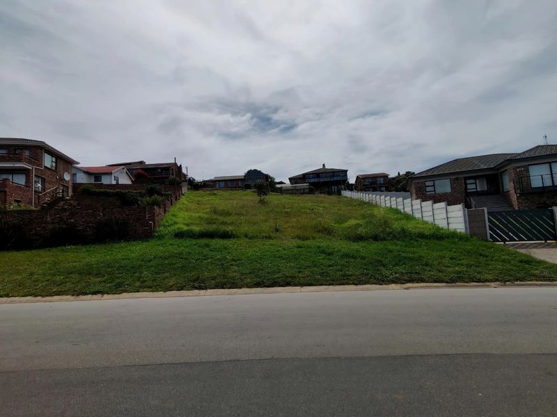 A vacant residential plot with a gentle upward slope, situated in an established neighborhood with surrounding boundary walls and street access.