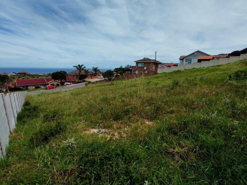 A vacant residential plot featuring a sloped landscape, enclosed by precast concrete boundary walls, situated in a developed neighbourhood with distant sea views.