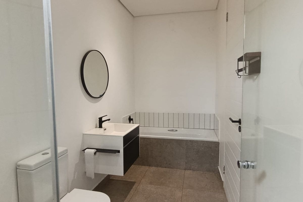 Modern bathroom featuring a wall-hung vanity, built-in bathtub, toilet, and neutral tiled flooring with clean, contemporary finishes.