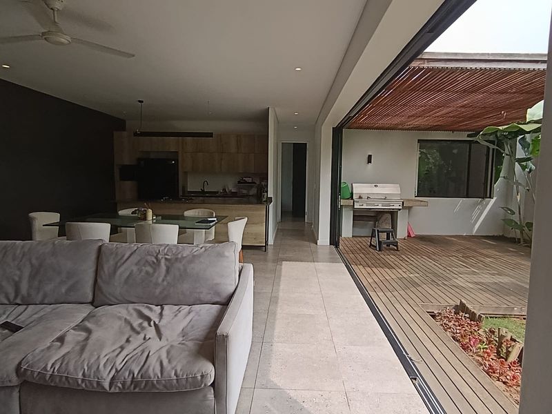 Modern open-plan living and kitchen area featuring seamless indoor-outdoor flow to a timber deck with a built-in barbecue and pergola.
