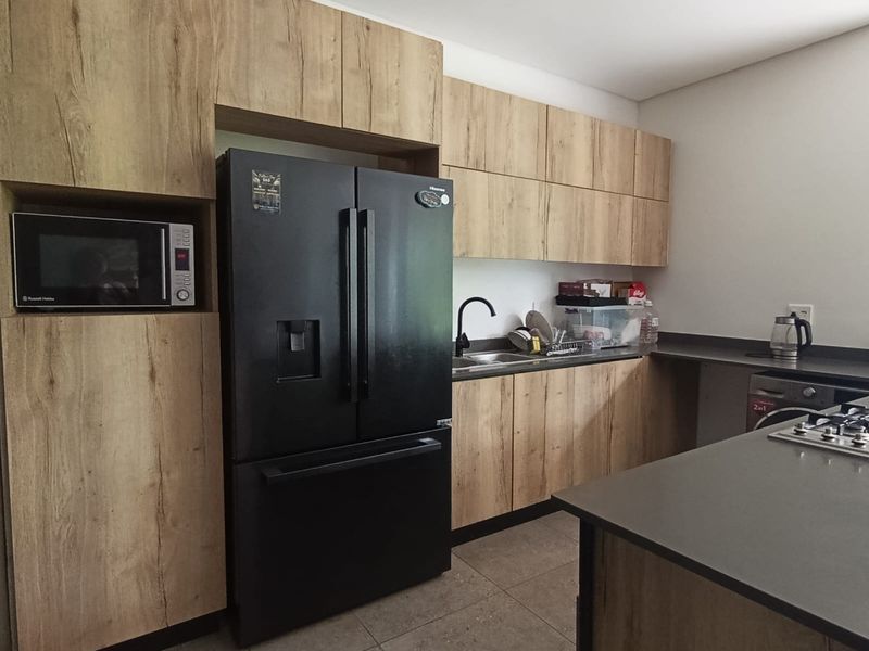 Modern kitchen featuring wood-look cabinetry, stone countertops, a built-in microwave, and a gas hob, offering a functional and contemporary cooking space.