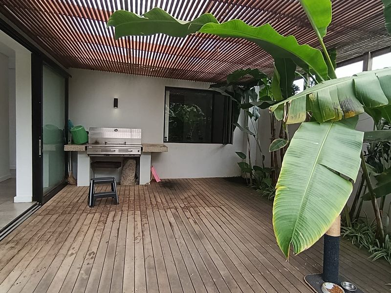 Covered outdoor patio featuring timber decking, a slatted pergola roof, and a built-in braai area with stone countertop, perfect for alfresco dining.