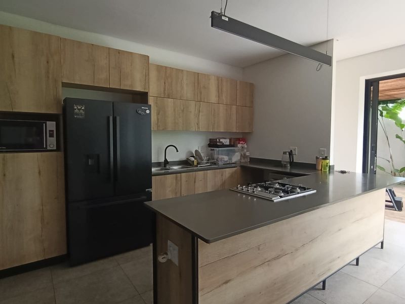 Modern kitchen featuring wood-finish cabinetry, a central island with a gas cooktop, stone countertops, and direct access to an outdoor patio area.