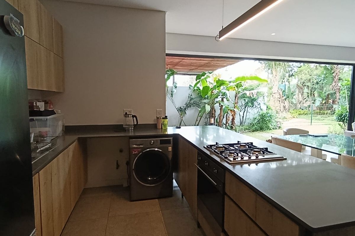 Modern kitchen featuring wood-finish cabinetry, stone countertops, a gas hob, and built-in oven, with seamless flow to an outdoor patio area.
