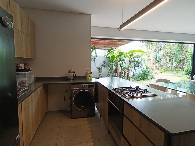 Modern kitchen featuring wood-finish cabinetry, stone countertops, a gas hob, and built-in oven, with seamless flow to an outdoor patio area.