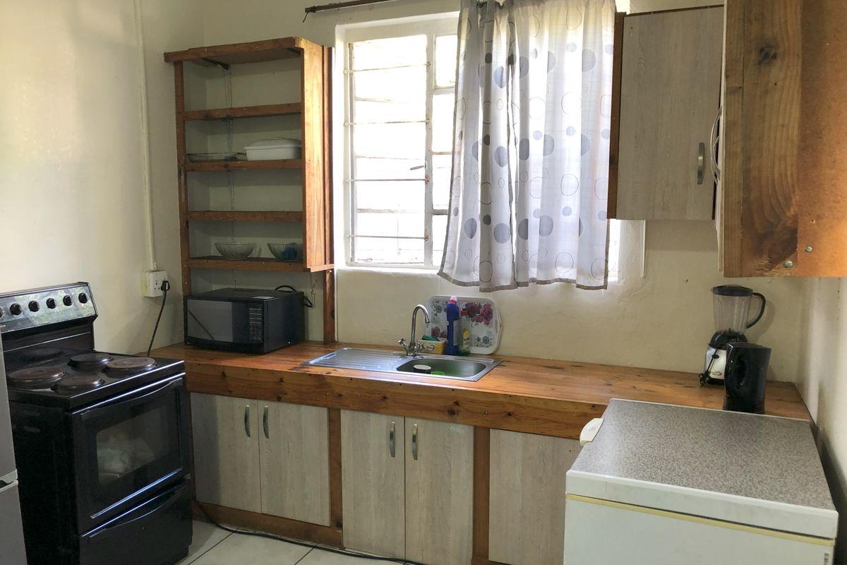 A functional kitchen featuring wooden countertops, built-in cabinetry, open shelving, and an electric stove, with tiled flooring and a window with security bars.
