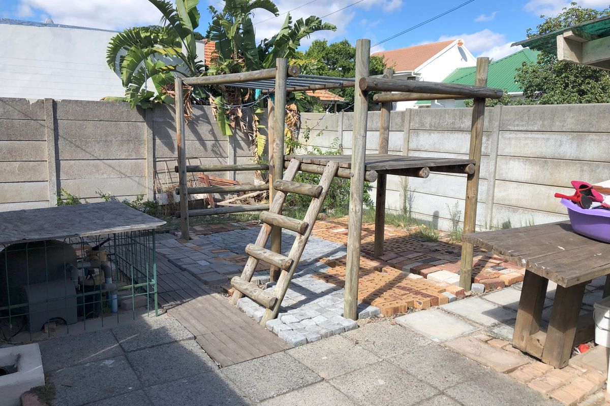Rear garden area featuring a paved patio, precast concrete boundary walls, and a wooden play structure.