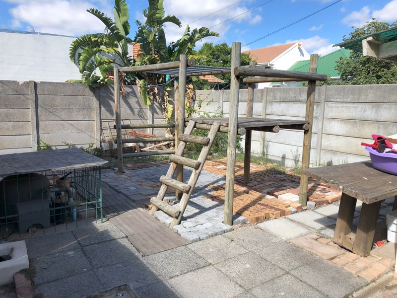 Rear garden area featuring a paved patio, precast concrete boundary walls, and a wooden play structure.