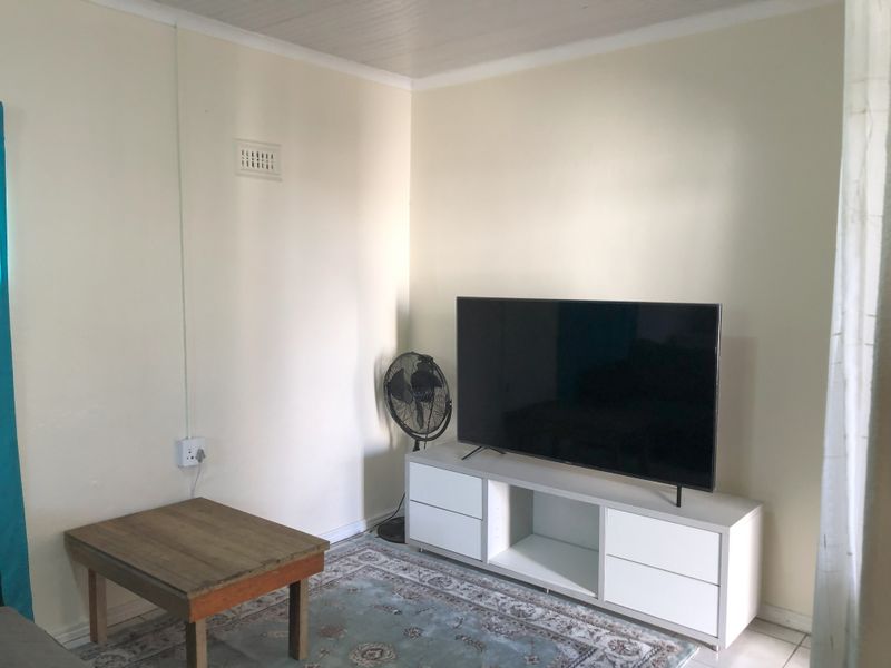 A simple living room area featuring neutral walls, a tongue and groove ceiling, and standard electrical fixtures.